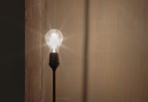 A single bulb gives off bright light, casting shadows on the walls behind it