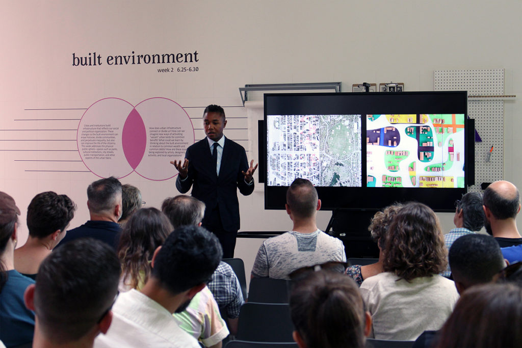 Speaker stands in front of "Built Environment" wall graphics while giving a presentation