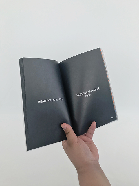 A hand holds a book open to two black pages with write text